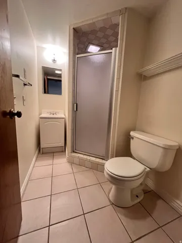 East  downstairs  3/4 bathroom featuring a frosted glass shower enclosure, tiled shower surround, and a vanity with an integrated sink
