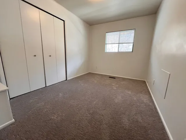 East Side - Bedroom featuring neutral carpeting, a double bi-fold closet, and a window with horizontal blinds