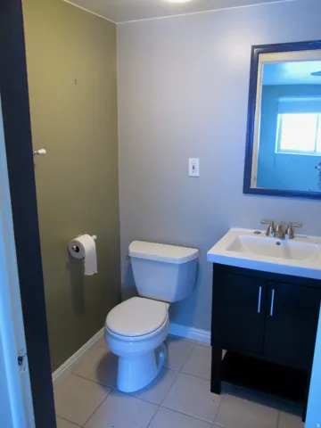 West Side - Full Bathroom with light-toned tiled flooring, a white toilet, and a dark wood-finish vanity with a white integrated sink