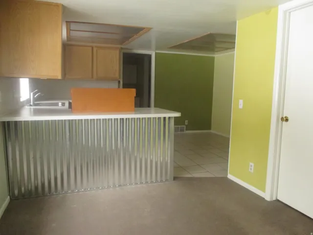West Side - Kitchen area featuring light wood-finish cabinetry, a stainless steel sink with a gooseneck faucet, and a breakfast bar with a corrugated metal facade