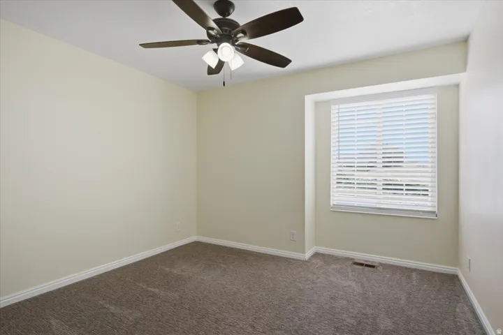 Carpeted room featuring a ceiling fan with integrated lighting, a window with horizontal blinds, and neutral-toned walls