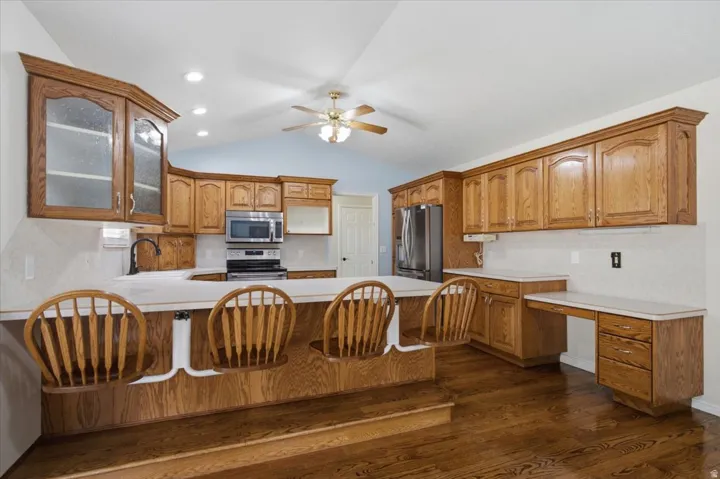 Spacious kitchen featuring rich wood cabinetry throughout, stainless steel appliances, white subway tile backsplash, and a large center island with wood-finish seating for three