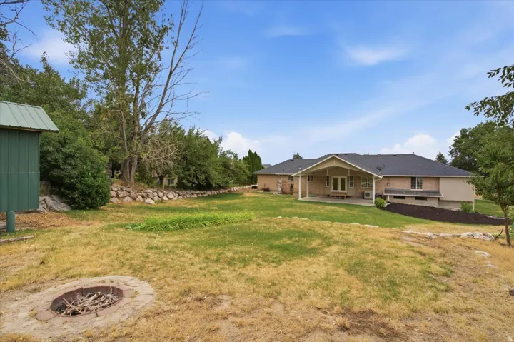 Expansive backyard featuring a built-in fire pit, mature trees, and a detached green shed