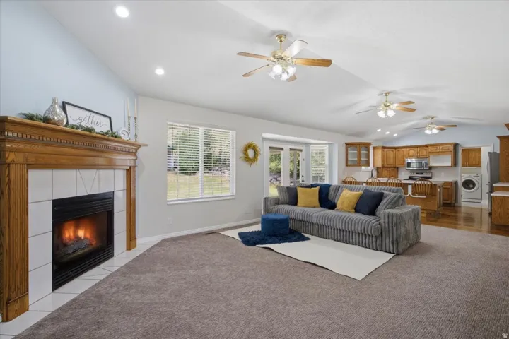 Living area featuring a fireplace with a wood mantel and tile surround, complemented by vaulted ceilings with recessed lighting and ceiling fans
