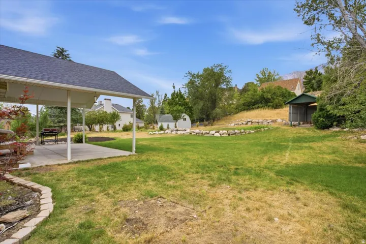 Expansive backyard featuring a covered patio, tiered landscaping with rock retaining walls, and a separate storage structure