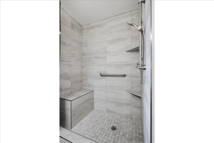 Tiled shower featuring a built-in bench, integrated wall niches, a brushed nickel shower head with handheld sprayer, and a grab bar