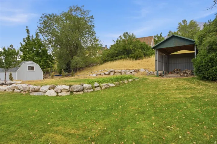 Expansive backyard featuring a manicured lawn, a large storage shed with a window, and a separate covered outbuilding