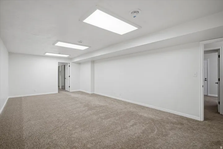 Spacious room featuring neutral carpet flooring, white walls, two rectangular ceiling light fixtures, and a ceiling-mounted smoke detector