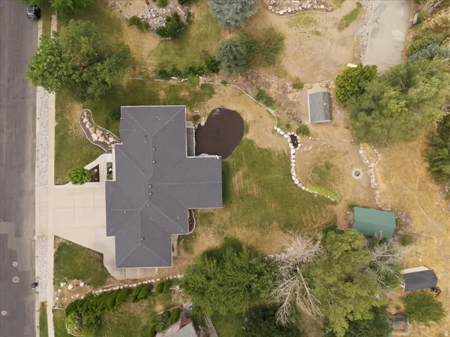 Expansive property featuring a multi-gabled roofline, concrete driveway, and a varied landscape design with mature trees and rock formations