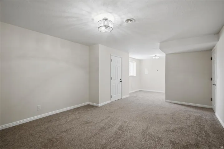 Spacious carpeted room featuring a decorative flush-mount light fixture, white trim, and a paneled door