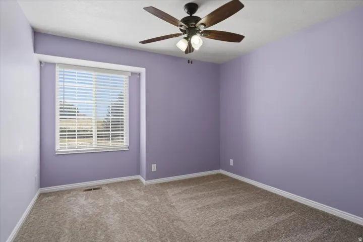 Carpeted room featuring a window with blinds, a ceiling fan with light fixture, and baseboard trim