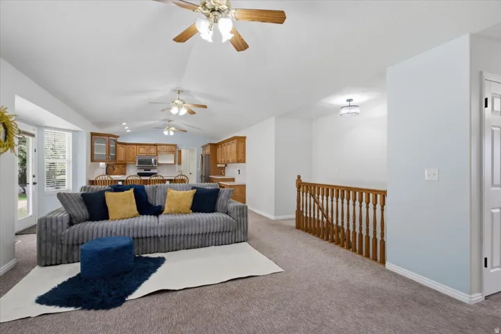 Open-concept living space featuring vaulted ceilings with multiple ceiling fans, light wood cabinetry, and a built-in kitchen island with seating