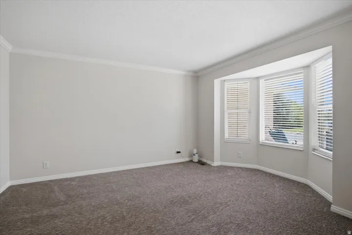 Bay window with white blinds, crown molding, light gray wall paint, and gray textured carpeting