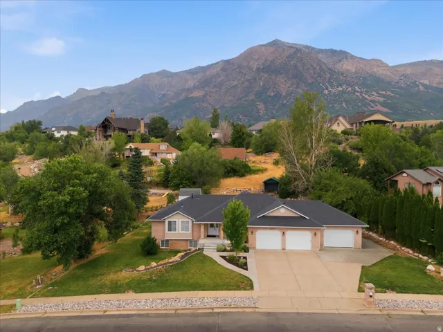 Brick residence with a prominent three-car garage and a two-car wide driveway, featuring a dark shingle roof and a mountain backdrop