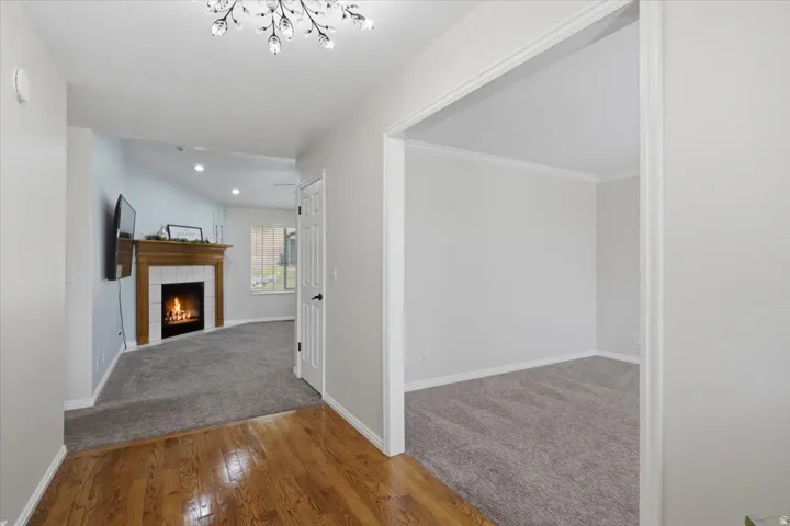 Entryway featuring hardwood flooring, leading to a carpeted living space with a fireplace and an additional carpeted room through an open archway