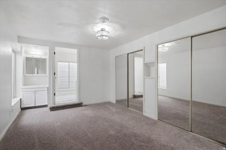 Spacious room featuring neutral carpeting, a built-in vanity with white cabinetry, mirrored sliding closet doors, and an overhead decorative light fixture