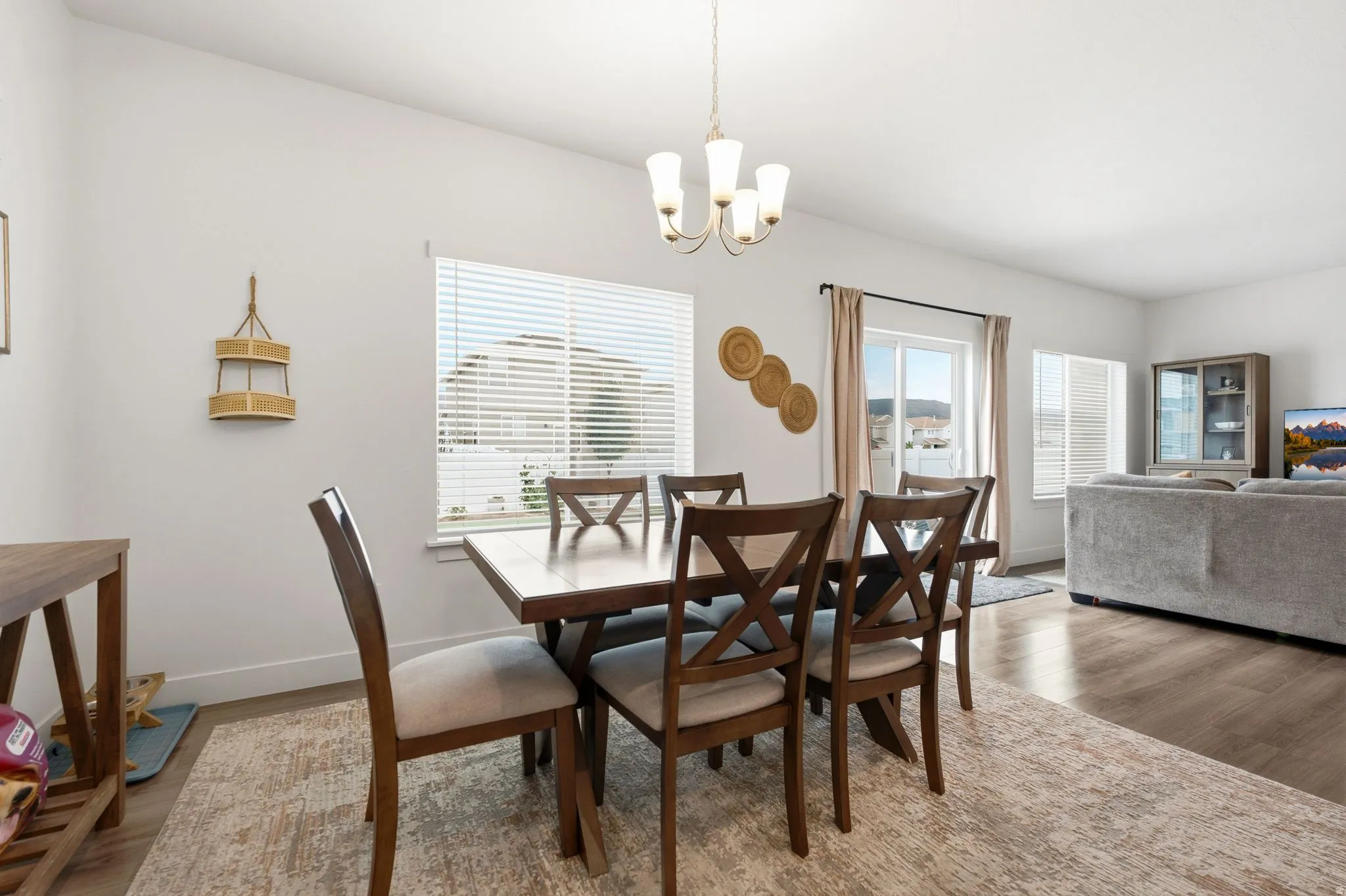 Open-concept living area featuring wood-finish flooring, a contemporary chandelier, large windows with blinds, a sliding glass door, and white walls