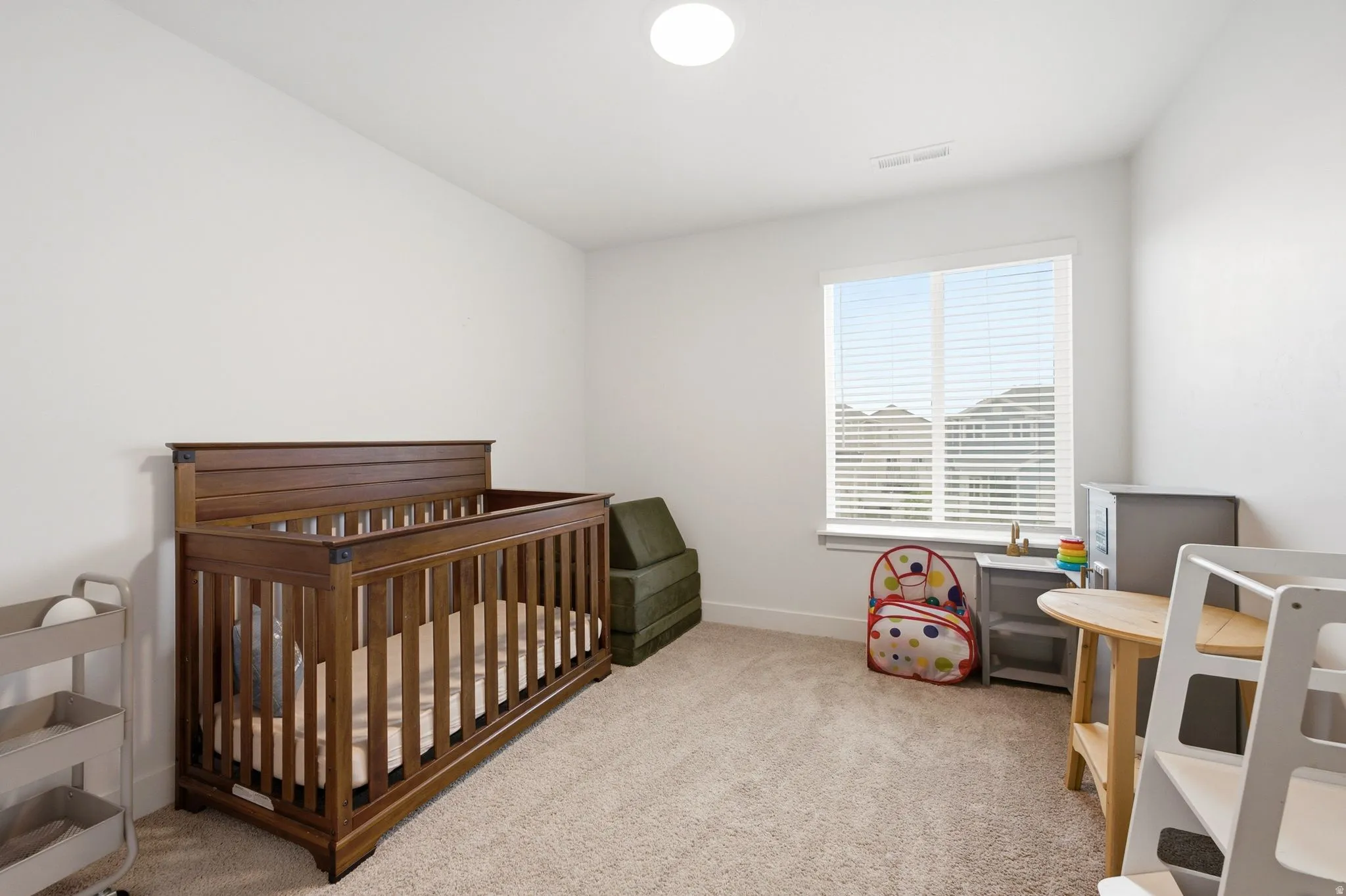 Bright interior space featuring neutral wall tones, carpet flooring, a window with horizontal blinds, and a flush mount ceiling light
