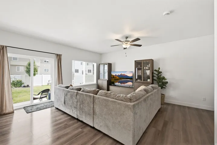 Living area featuring wood-finish flooring, a ceiling fan with integrated lighting, and a sliding glass door providing direct outdoor access to the backyard