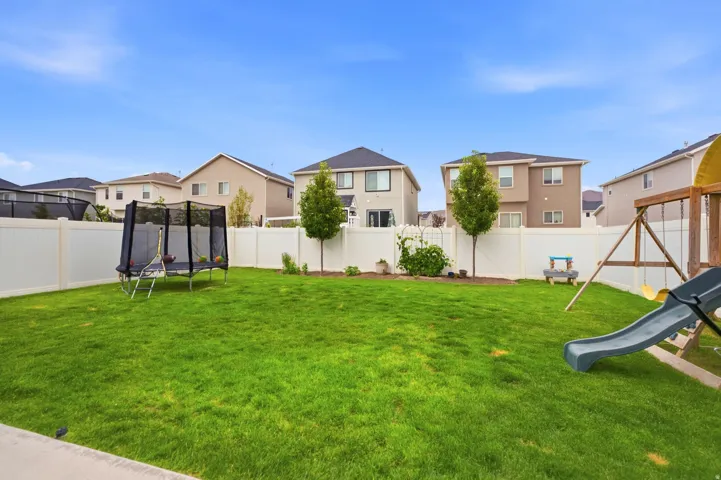 Expansive backyard featuring a manicured lawn, white privacy fencing, and mature landscaping