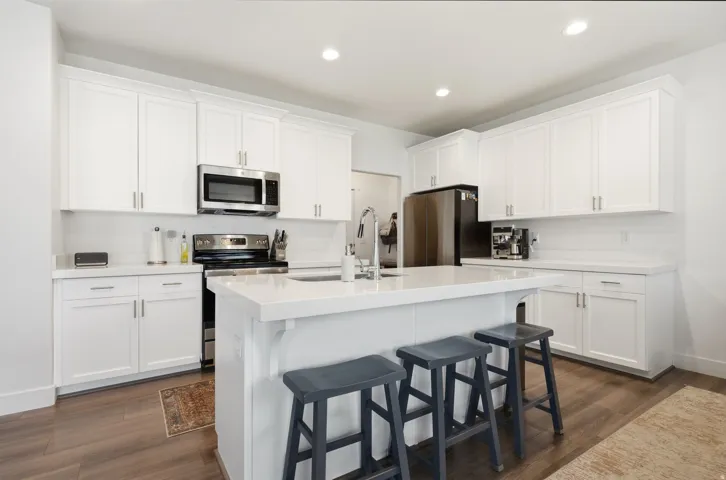 Modern kitchen featuring white shaker cabinetry, stainless steel appliances, a center island with a breakfast bar, recessed lighting, and wood-finish flooring