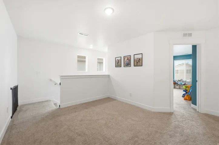 Carpeted landing area featuring a white railing, recessed lighting, and a doorway with white trim