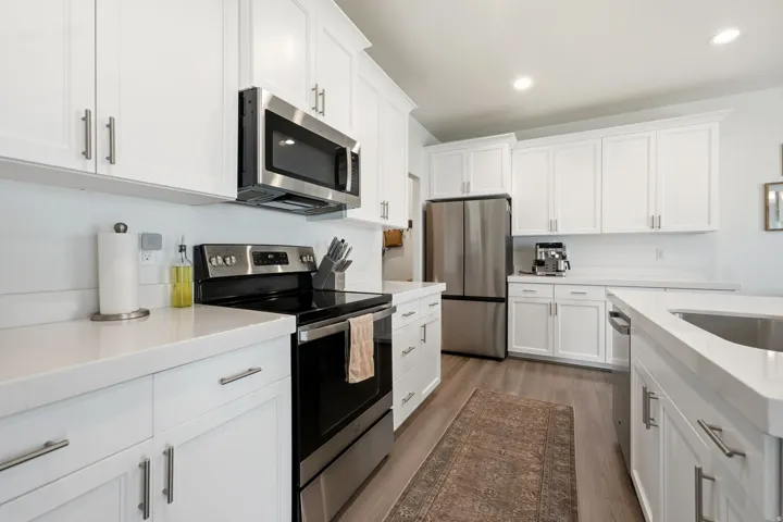 Kitchen featuring white shaker cabinetry, stainless steel appliances, light-toned countertops, wood-finish flooring, and recessed lighting