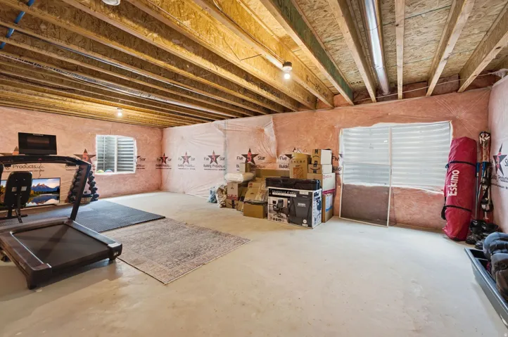 Unfinished basement space featuring exposed wood joists, concrete flooring, and multiple windows