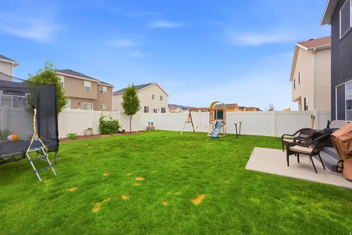 Expansive green lawn with a concrete patio, mature trees, and a white vinyl privacy fence