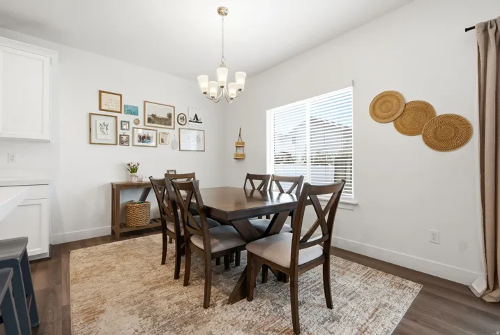 Dining area with wood-finish flooring, a contemporary chandelier, and a window featuring blinds