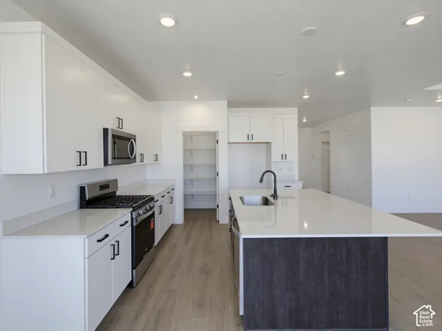 Kitchen featuring white cabinetry with matte black hardware, stone-finish countertops, a center island with a stainless steel sink and matte black faucet, integrated stainless steel appliances, and wood-finish flooring