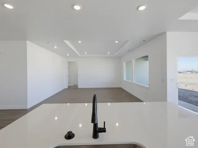 Kitchen island featuring a quartz countertop and a matte black pull-down faucet, recessed ceiling lighting, tray ceiling detail, wood-finish flooring, and expansive windows