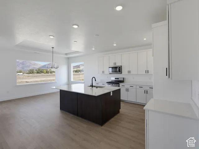 Kitchen featuring white cabinetry, quartz countertops, a dark-finish center island, recessed lighting, and wood-finish flooring