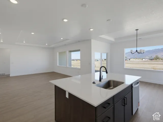 Kitchen island with quartz countertop, under-mount stainless steel sink, dark cabinetry, recessed lighting, and wood-finish flooring