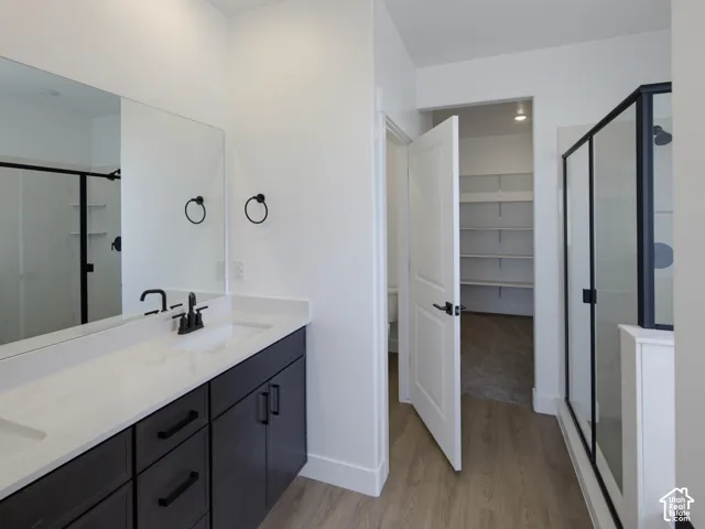 Bathroom featuring a dark-finish double vanity with a light-tone countertop, matte black fixtures, a wall-to-wall mirror, and a glass-enclosed shower with a matte black frame
