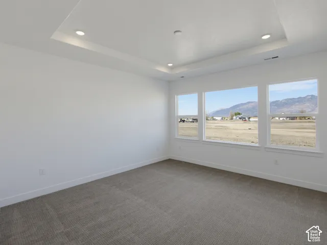 Room featuring a tray ceiling, recessed lighting, wall-to-wall carpeting, and large windows with a mountain backdrop