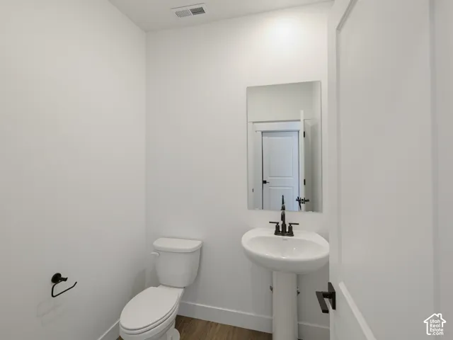 Pedestal sink with matte black faucet, wall-mounted mirror, wood-finish flooring, and matte black hardware