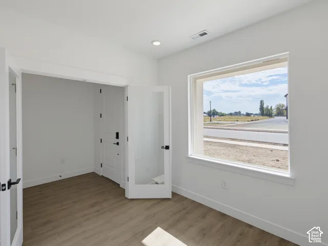 Wood-finish flooring, white walls, large picture window, and interior French doors with glass panes and matte black hardware