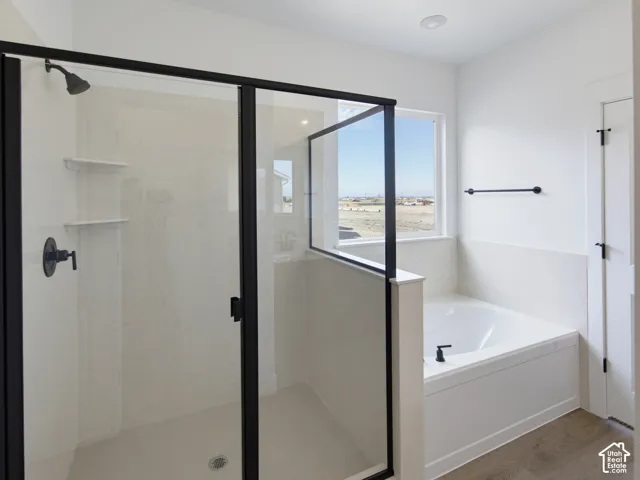 Walk-in shower with matte black fixtures and glass enclosure, soaking tub, light-toned wall tile, and wood-finish flooring