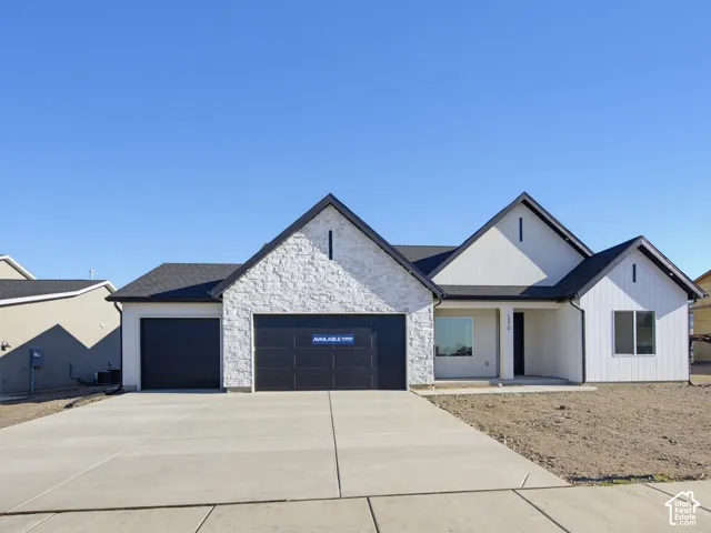 Modern exterior featuring white vertical siding, light stone masonry accents, multiple gabled rooflines, and a concrete driveway leading to a three-car garage