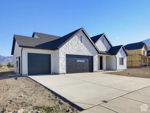 Exterior featuring a stone facade, dual garage doors, high-pitched gables, and concrete driveway