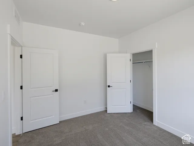Room featuring neutral wall-to-wall carpeting, two-panel interior doors, matte black hardware, and a built-in closet with integrated shelving