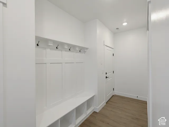 Built-in mudroom bench with integrated lower cubbies, white board-and-batten wall detailing, overhead shelf, matte black hardware, and wood-finish flooring