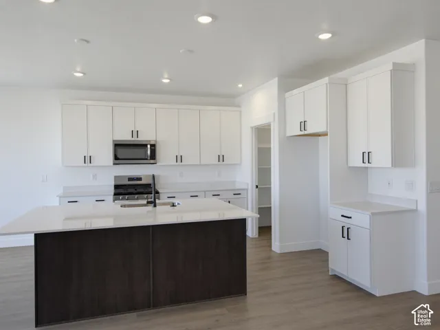 Kitchen featuring white shaker-style cabinetry, quartz countertops, a dark-finish center island, recessed ceiling lighting, and wood-finish flooring