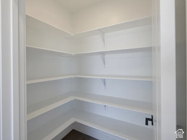 Walk-in storage space featuring wrap-around white shelving, support brackets, and dark wood-finish flooring