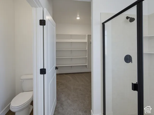 Walk-in shower with matte black fixtures and glass enclosure, porcelain commode, and built-in shelving unit