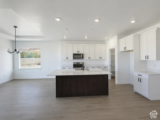 Kitchen featuring white shaker-style cabinetry, dark-toned center island, white quartz countertops, recessed lighting, and wood-finish flooring
