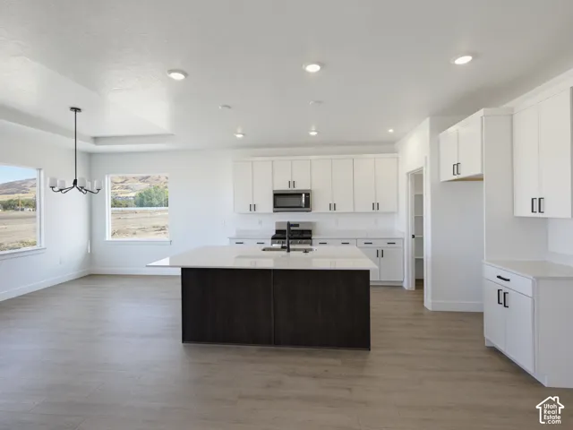Kitchen featuring a central island with a contrasting dark base, white cabinetry with matte black hardware, stone-finish countertops, recessed lighting, and wood-finish flooring