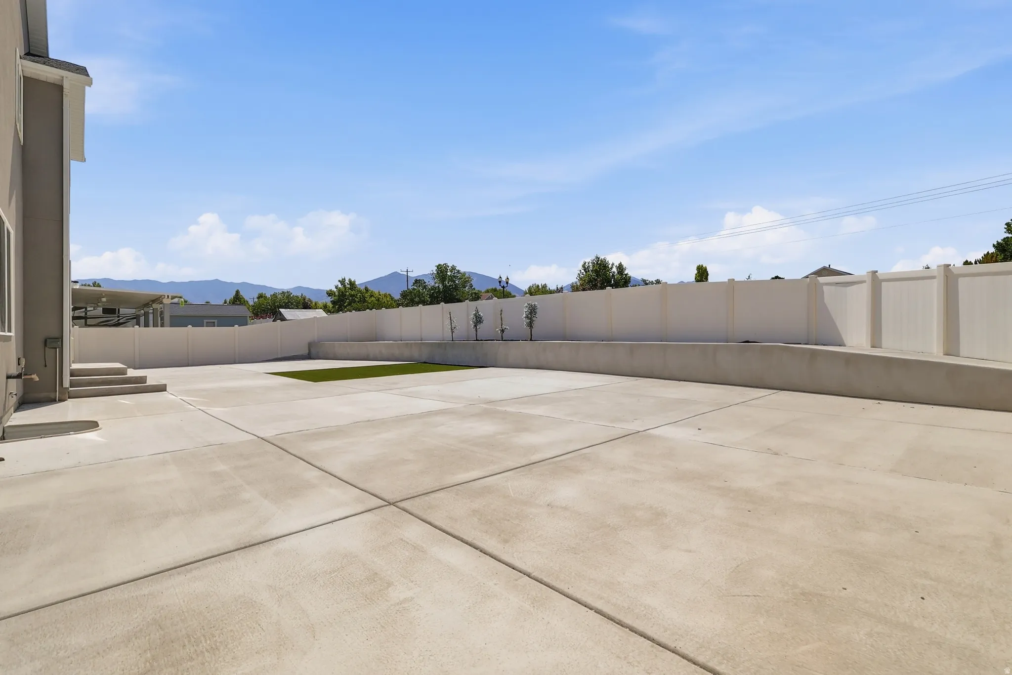 Expansive concrete patio area with a section of artificial turf and young trees
