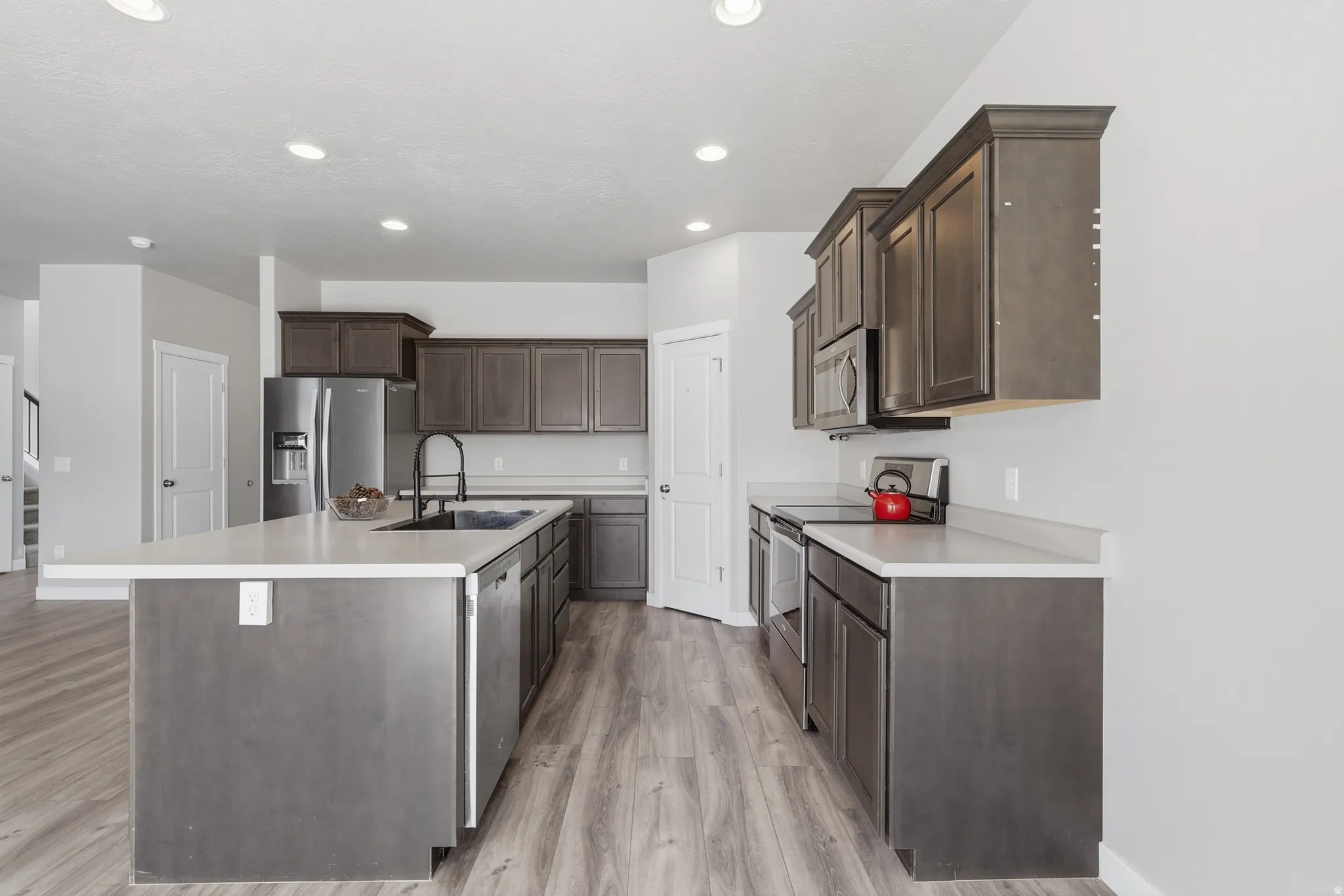 Expansive kitchen featuring a large island with countertop seating, wood-finish flooring, stainless steel appliances, dark wood cabinetry, and recessed lighting